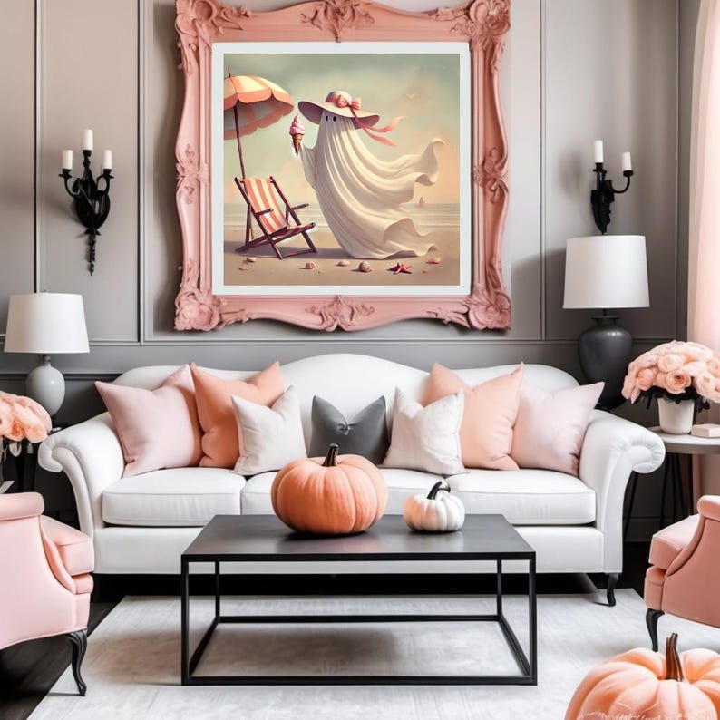 May include: A framed artwork depicts a whimsical ghost enjoying a beach day, wearing a hat and holding an ice cream cone. The artwork is framed in a pink ornate frame, above a white sofa with pink and gray pillows. A black coffee table holds pumpkins.