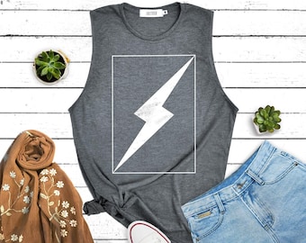 May include: A grey vest top featuring a white lightning bolt design within a white frame. The image includes denim shorts, white trainers, and a brown scarf with floral embroidery. Two small potted succulents are also visible.