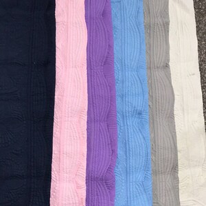 Puede incluir: Siete mantas acolchadas en varios colores, incluyendo azul marino, rosa, morado, azul claro, gris y blanco. Las mantas tienen un borde festoneado decorativo.