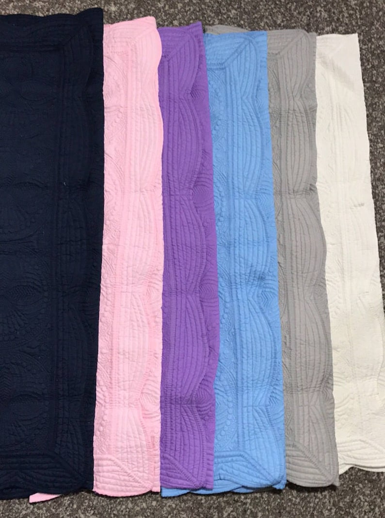 Puede incluir: Siete mantas acolchadas en varios colores, incluyendo azul marino, rosa, morado, azul claro, gris y blanco. Las mantas tienen un borde festoneado decorativo.