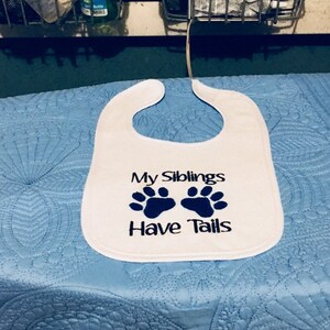 May include: White baby bib with blue paw prints and the text "My Siblings Have Tails".