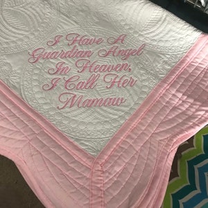 May include: White quilted blanket with pink trim and the embroidered text: "I Have a Guardian Angel In Heaven, I Call Her Mamaw." The blanket features a detailed circular pattern.