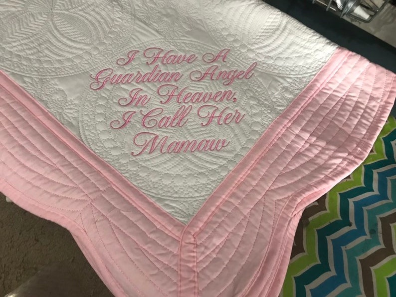 May include: White quilted blanket with pink trim and the embroidered text: "I Have a Guardian Angel In Heaven, I Call Her Mamaw." The blanket features a detailed circular pattern.