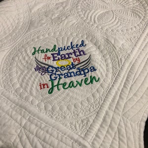 May include: White quilted blanket with detailed stitching. The blanket has embroidered text in various colours: "Handpicked for Earth by My Great Grandpa in Heaven". The design includes angel wings and a halo.