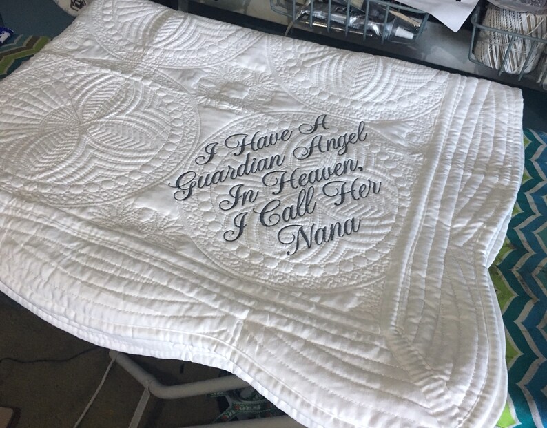 Puede incluir: Manta acolchada blanca con el texto bordado "Tengo un &aacute;ngel de la guarda en el cielo, la llamo Nana".