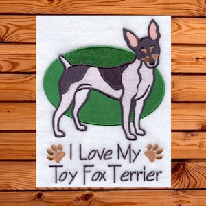 Puede incluir: Diseño bordado de un perro Toy Fox Terrier en negro, blanco y marrón, sobre un óvalo verde. El texto "I Love My Toy Fox Terrier" está debajo, con huellas de patas a cada lado. El diseño está sobre un fondo blanco.
