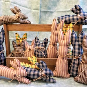 May include: A collection of handmade patchwork bunny rabbits in various colors and patterns, including blue, brown, yellow, and red plaid, sitting on a wooden shelf.