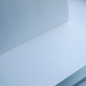 May include: A blank, white notebook with a spine and a few pages visible. The notebook is open and lying flat on a white surface.