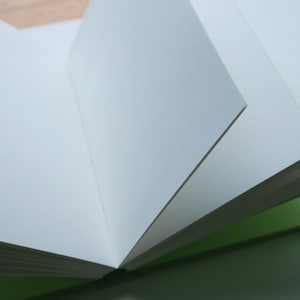 May include: A white blank notebook with a green cover. The notebook is open and the pages are fanned out.