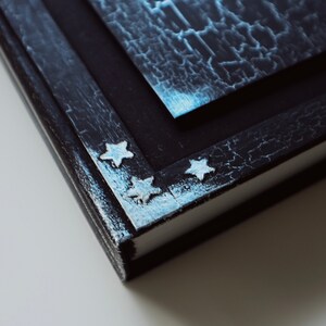 Puede incluir: Primer plano de un diario encuadernado en cuero negro con un acabado desgastado. Los bordes del diario est&aacute;n decorados con estrellas plateadas.