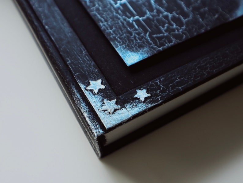 Puede incluir: Primer plano de un diario encuadernado en cuero negro con un acabado desgastado. Los bordes del diario est&aacute;n decorados con estrellas plateadas.