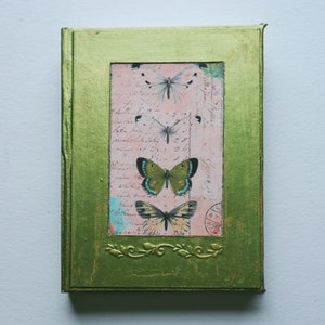 May include: A green journal with a gold frame and a pink and white butterfly design. The journal has a vintage look and feel.