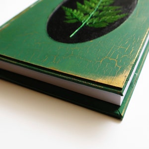May include: A green journal with a gold trim and a pressed fern on the cover.