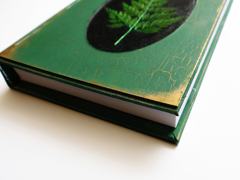 May include: A green journal with a gold trim and a pressed fern on the cover.