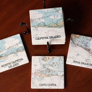 May include: Set of six ceramic coasters featuring nautical maps of various Florida islands. The coasters are white with blue and brown details. The maps include "North Captiva Island", "Captiva Island", "Boca Grande", and "Cayo Costa".