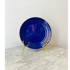 May include: A blue ceramic plate with a rippled design, displayed on a gold metal stand.