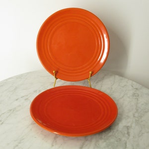 May include: Two orange ceramic dinner plates with a ridged design. The plates are stacked on top of each other.