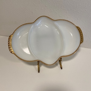 May include: A white milk glass serving dish with a gold beaded rim and three sections. The dish is on a metal stand with three legs.