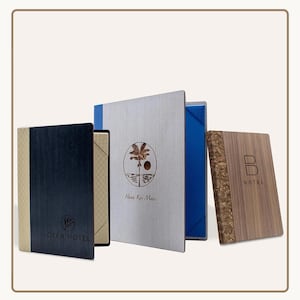 May include: A collection of four menu covers with various designs. One is dark wood with a gold accent and the "OLEA HOTEL" logo. Another has a silver cover with a palm tree logo and "Hana Kai Maui" text. The third is wood with a "B HOTEL" logo.