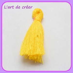 May include: A bright yellow tassel with a knotted top. The tassel is made of soft yarn and is approximately 2 inches long.