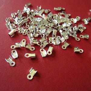 Op de afbeelding: Een grote hoeveelheid zilverkleurige metalen sluitingen voor het maken van sieraden. De sluitingen zijn klein en hebben een eenvoudig ontwerp.