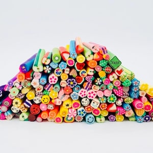 Peut inclure: Un grand tas de bâtonnets en pâte polymère multicolores disposés en monticule triangulaire. Chaque tige cylindrique présente des motifs complexes en coupe transversale, incluant des fruits, fleurs, visages souriants et formes géométriques.