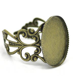 May include: A bronze ring setting with an oval-shaped bezel for a cameo or other decorative element. The ring setting has a delicate, ornate design.