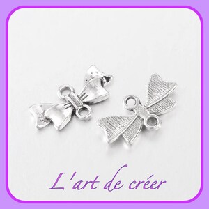 Op de afbeelding: Twee zilveren metalen bedels in de vorm van een strik met een lus aan elke kant. De bedels zijn ontworpen om te worden gebruikt als sieradenbevindingen of versieringen.