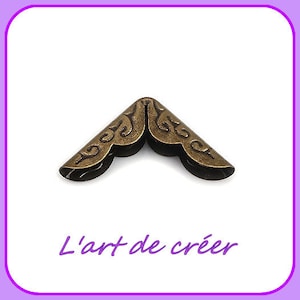 May include: A gold metal corner protector with a decorative design. The corner protector is shaped like a triangle with rounded edges.