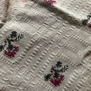 Peut inclure: Un tissu blanc tiss&eacute; avec un motif textur&eacute; et des fleurs brod&eacute;es noires et rouges.