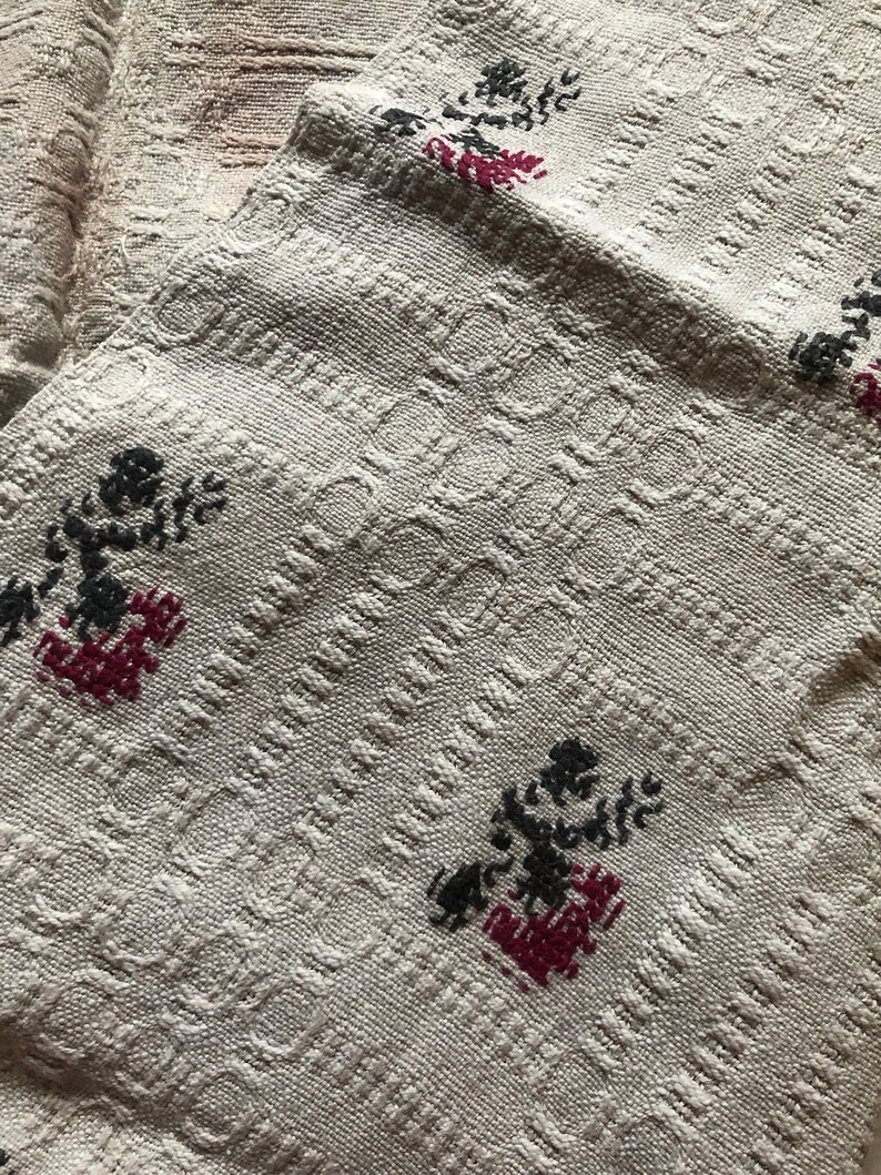 Peut inclure: Un tissu blanc tiss&eacute; avec un motif textur&eacute; et des fleurs brod&eacute;es noires et rouges.