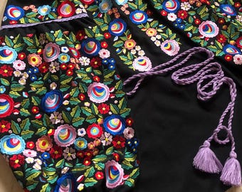 May include: Black embroidered blouse with colorful floral patterns and a purple tassel tie.