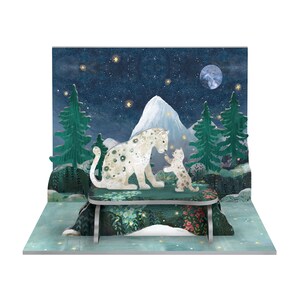 May include: A 3D pop-up card depicting a snowy mountain scene with a mother and baby snow leopard. The animals are white with black spots and are seated on a green and floral patterned table. The background is a dark blue sky with white stars and a full moon.