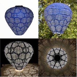 May include: A blue solar-powered lantern with a white floral pattern. The lantern is hanging from a tree branch and casting a pattern of light on the ground.
