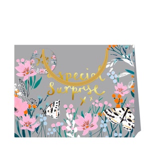 May include: A gray gift bag with a floral pattern featuring pink flowers, butterflies, and green leaves. The bag has a gold handle and the text "a special surprise" in gold lettering.