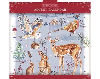 Può includere: Un calendario dell'avvento blu e bianco con una scena di foresta invernale. Il calendario presenta illustrazioni di un cervo, un gufo, un fagiano, un riccio e conigli. Il testo "PAPER HOUSE ADVENT CALENDAR" è stampato in alto.