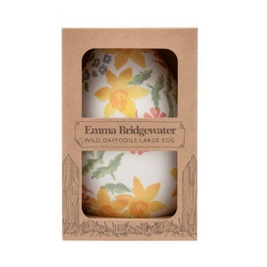 May include: A large, egg-shaped ceramic piece with a floral design featuring yellow daffodils, green leaves, and other colorful flowers. The egg is packaged in a brown cardboard box. The text "Emma Bridgewater WILD DAFFODILS LARGE EGG" is printed on the box.