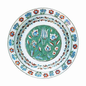May include: A white ceramic plate with a green centre featuring a floral design with blue, red and white flowers. The plate has a white border with a blue and red floral design.