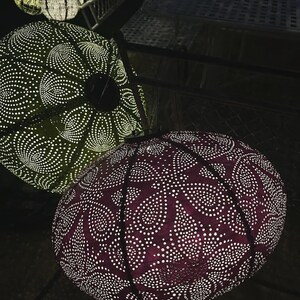 Puede incluir: Dos linternas redondas con patrones y luces blancas que brillan a trav&eacute;s. La linterna superior es verde con un patr&oacute;n blanco, y la linterna inferior es morada con un patr&oacute;n blanco.