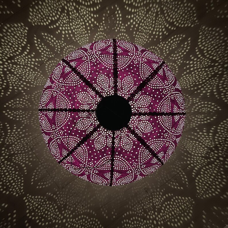 Puede incluir: Una pantalla de l&aacute;mpara de color morado con un patr&oacute;n geom&eacute;trico de puntos blancos y un centro negro. La pantalla proyecta una sombra en el techo.