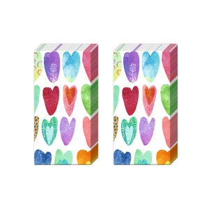 May include: Two packs of tissue paper featuring a colourful heart design. Each pack has a white background with a variety of coloured hearts, including red, pink, purple, blue, green, and yellow. The hearts are arranged in a repeating pattern.