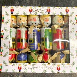 May include: A box of 12 party crackers, each decorated with festive images of Santa Claus and toy soldiers. The crackers are cylindrical and tied with gold ribbons. The box has a white background with a pattern of nutcrackers and greenery, and the brand name "Caspari".