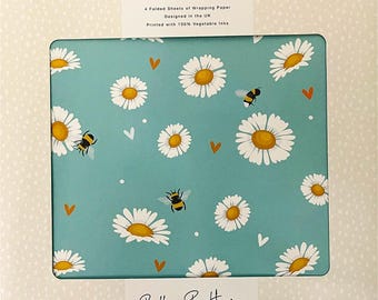 May include: A gift wrap set featuring a teal background with a pattern of white daisies, orange hearts, and bumblebees. The packaging includes the text "LUXURY ECO GIFT WRAP" and "Belly Button DESIGNS". The set includes 4 sheets and 2 tags.