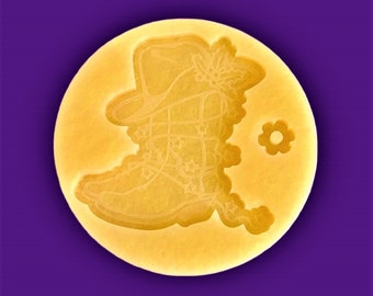 May include: A yellow silicone mold with a design of a boot with a flower on top. The mold is round and has a small flower design on the side.
