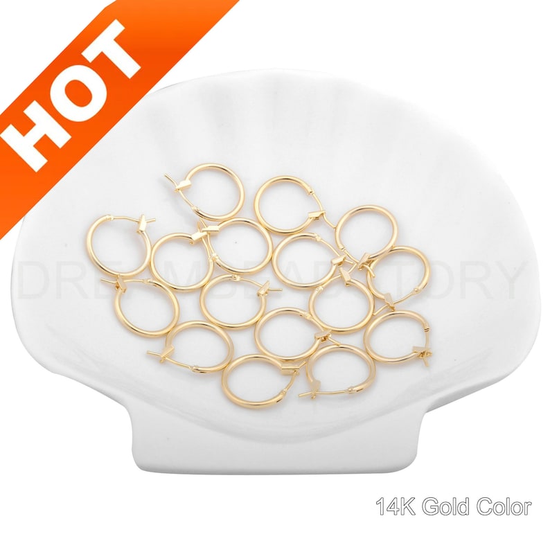 May include: A group of 14K gold-colored hoop earrings on a white seashell-shaped surface.