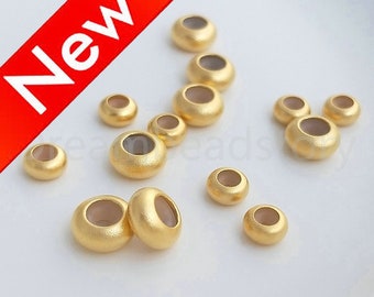 May include: A close-up of a group of gold-colored metal beads. The beads are round and have a hole in the center. They are arranged in a semi-circle on a white surface.