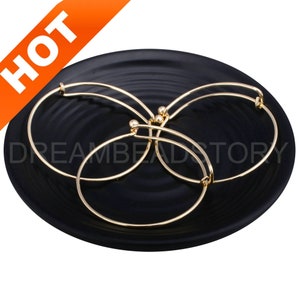 May include: Three gold-toned bangle bracelets with a small bead accent on each. The bracelets are displayed on a black circular plate.