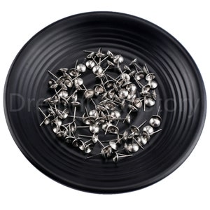 May include: A black plate filled with silver metal dome head tacks. The tacks have a small, pointed end and a round, flat head.