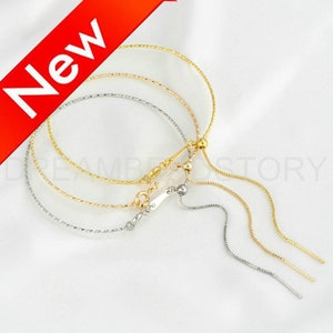 Può includere: Tre braccialetti regolabili a catena dorata e argentata con una perla scorrevole e un pon pon. I braccialetti sono realizzati con una catena delicata con una finitura testurizzata.
