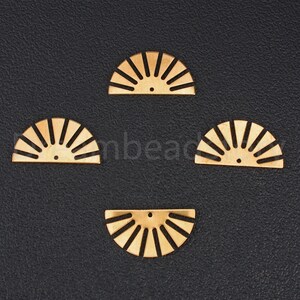 May include: Four gold-colored metal sunburst shapes, each with a hole in the center. The sunbursts are arranged in a diamond pattern on a black background.